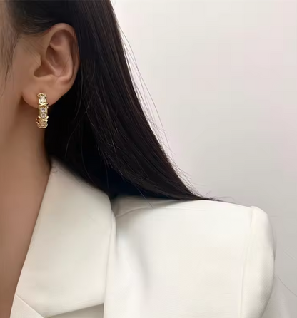 Aros huggies dorados con zirconia AAA diseño cruzado X-Twirl

Detalle de engaste cruzado en aros dorados con brillo

Aretes huggie chapados en oro 18K sobre superficie de madera

Modelo usando aros huggies dorados tamaño 20 mm